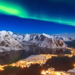 Vista panorámica de Bodø, Noruega, con su catedral de estilo funcionalista y montañas nevadas en el fondo, bajo el cielo ártico.