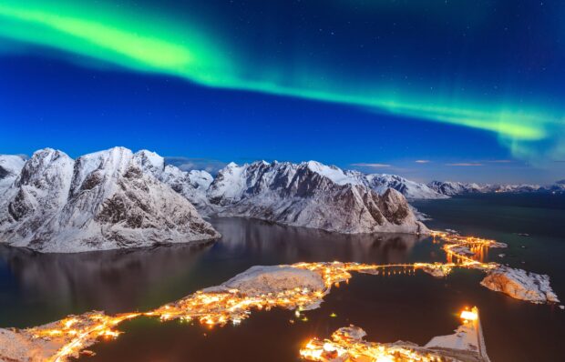 Vista panorámica de Bodø, Noruega, con su catedral de estilo funcionalista y montañas nevadas en el fondo, bajo el cielo ártico.